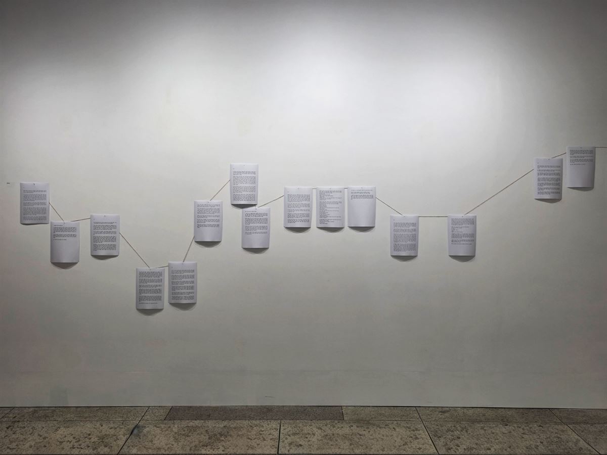 글이 인쇄된 종이 여러 장이 끈에 매달려 벽을 따라 물결처럼 이어진 설치